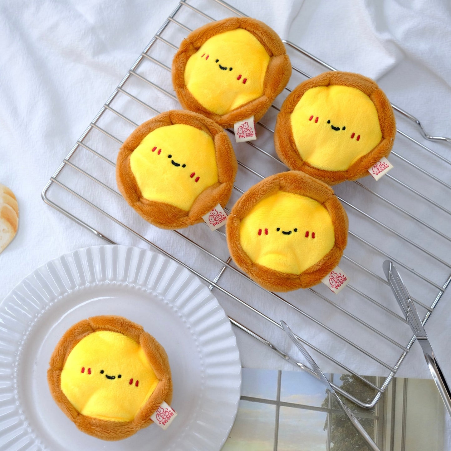 Plush pastry toys with smiling faces on a cooling rack and plate.