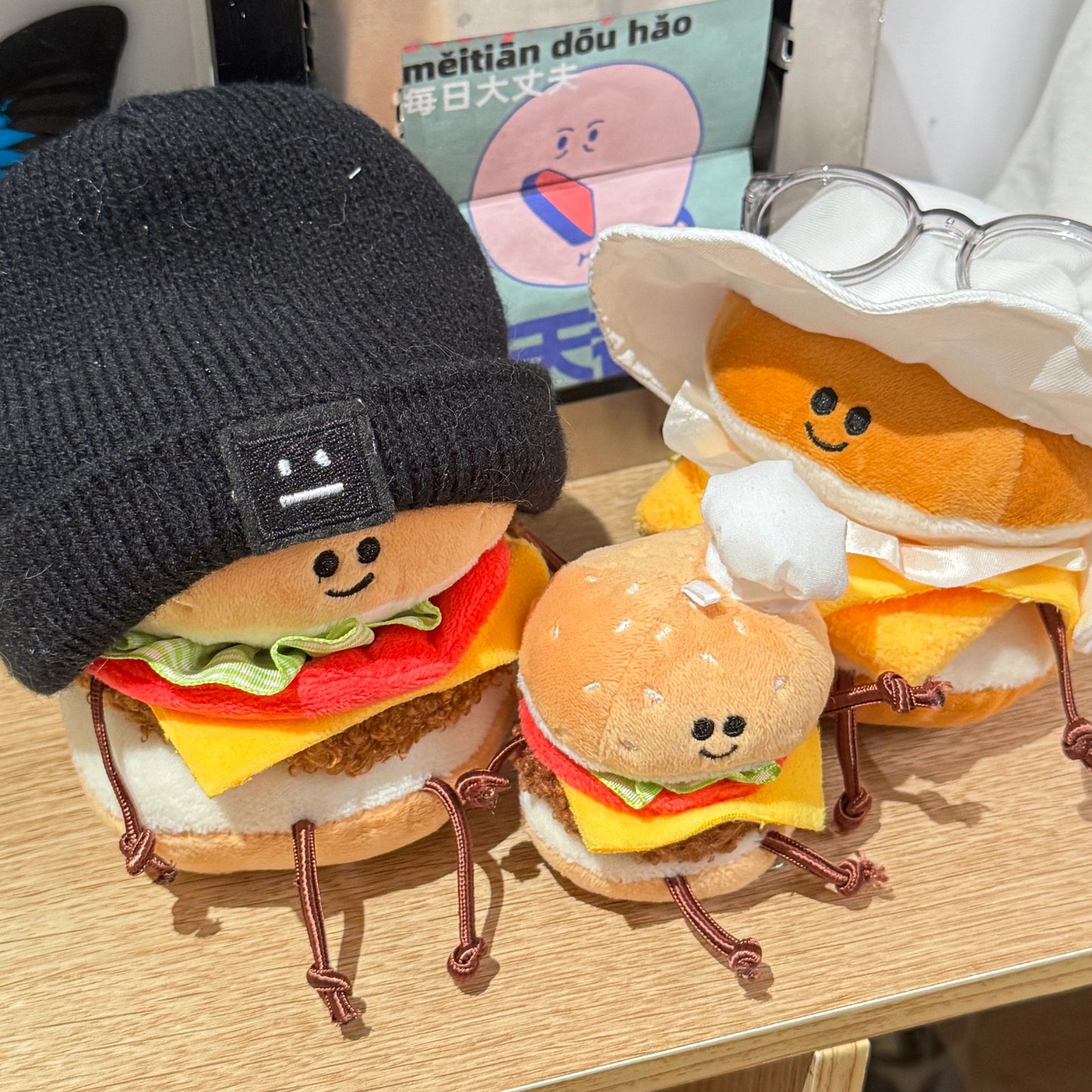 Plush toys shaped like hamburgers and buns on a wooden surface with a small box in the background.