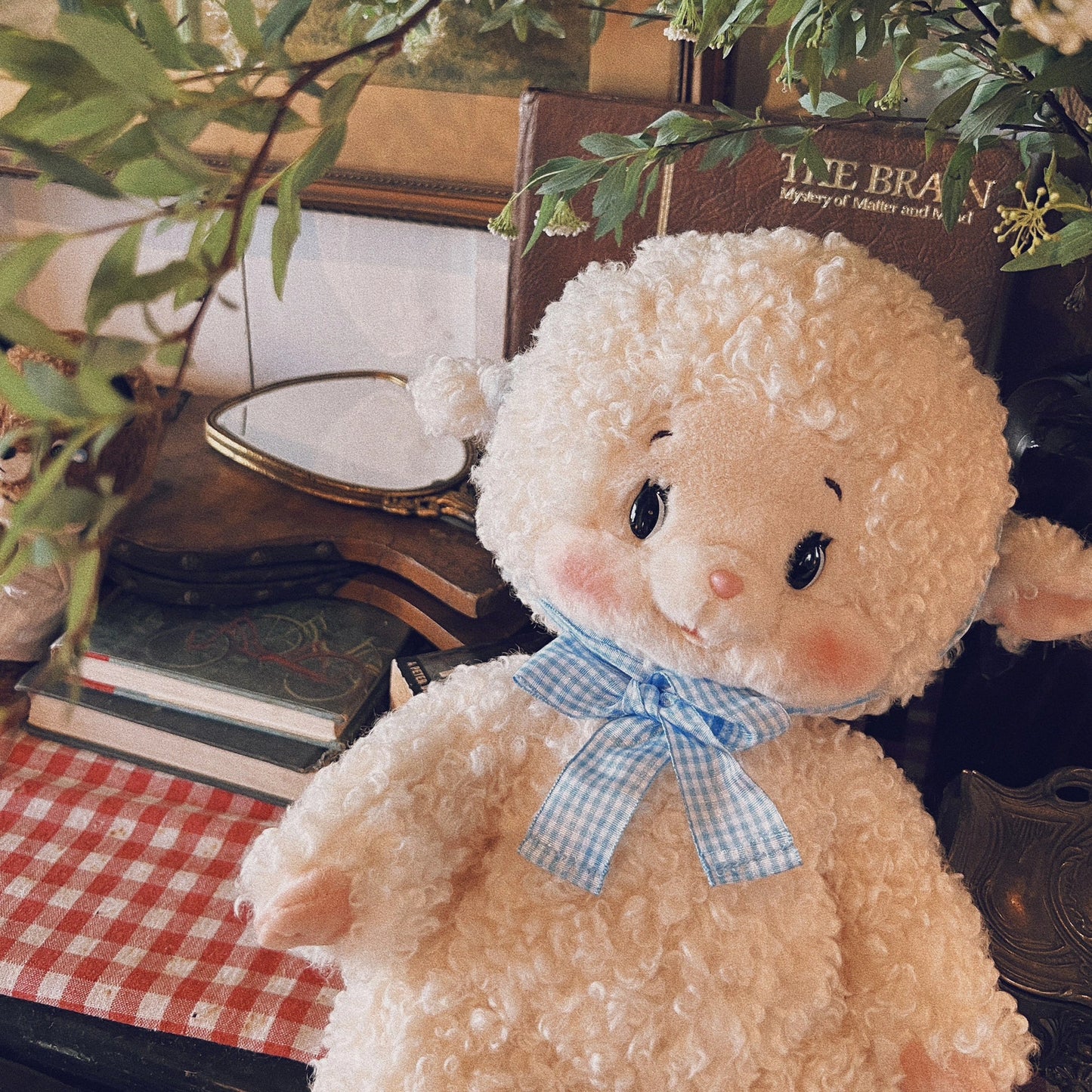 Stuffed animal with a blue bow tie on a table with books and plants