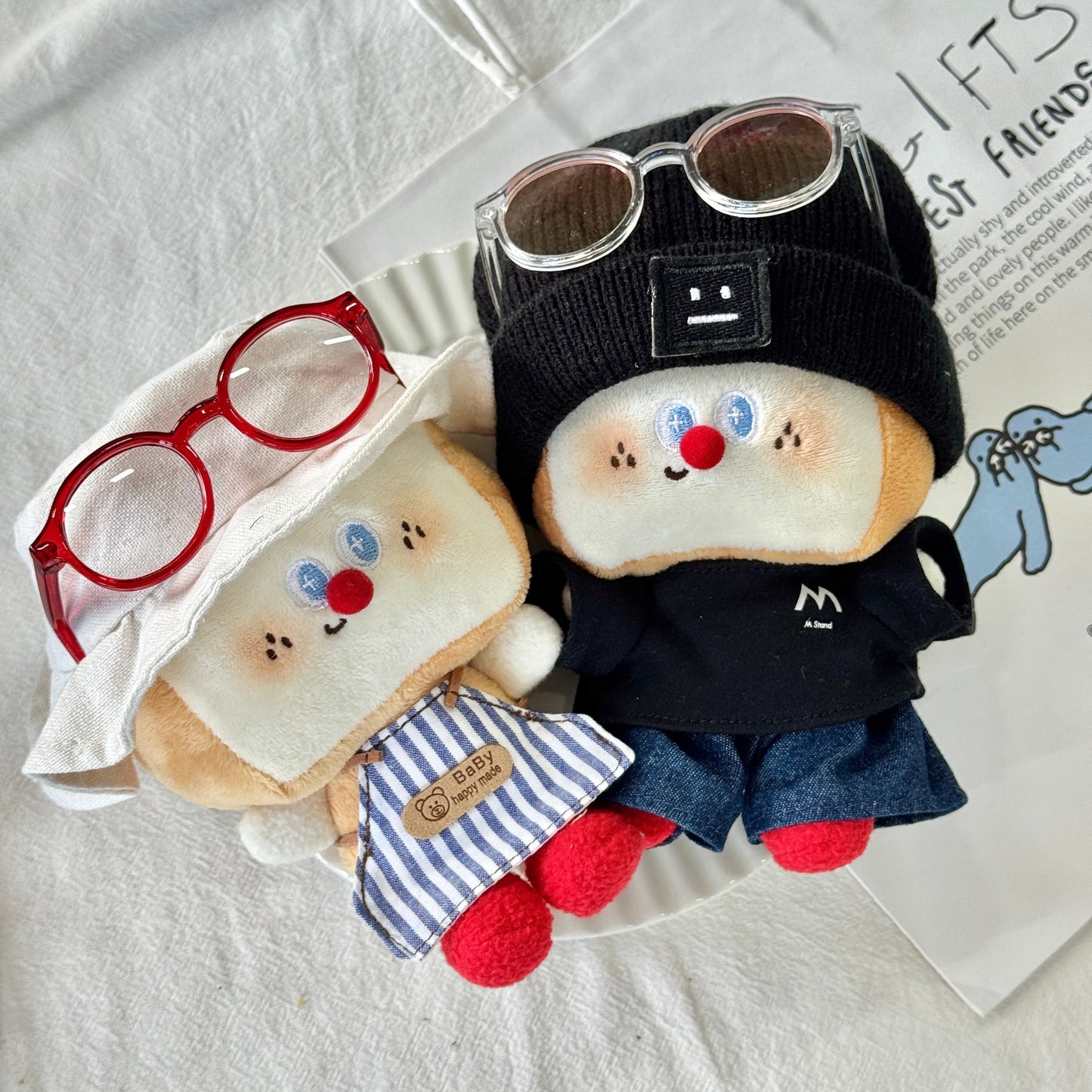 Two plush toys resembling sandwiches with faces, one wearing goggles and a black outfit, on a white surface.
