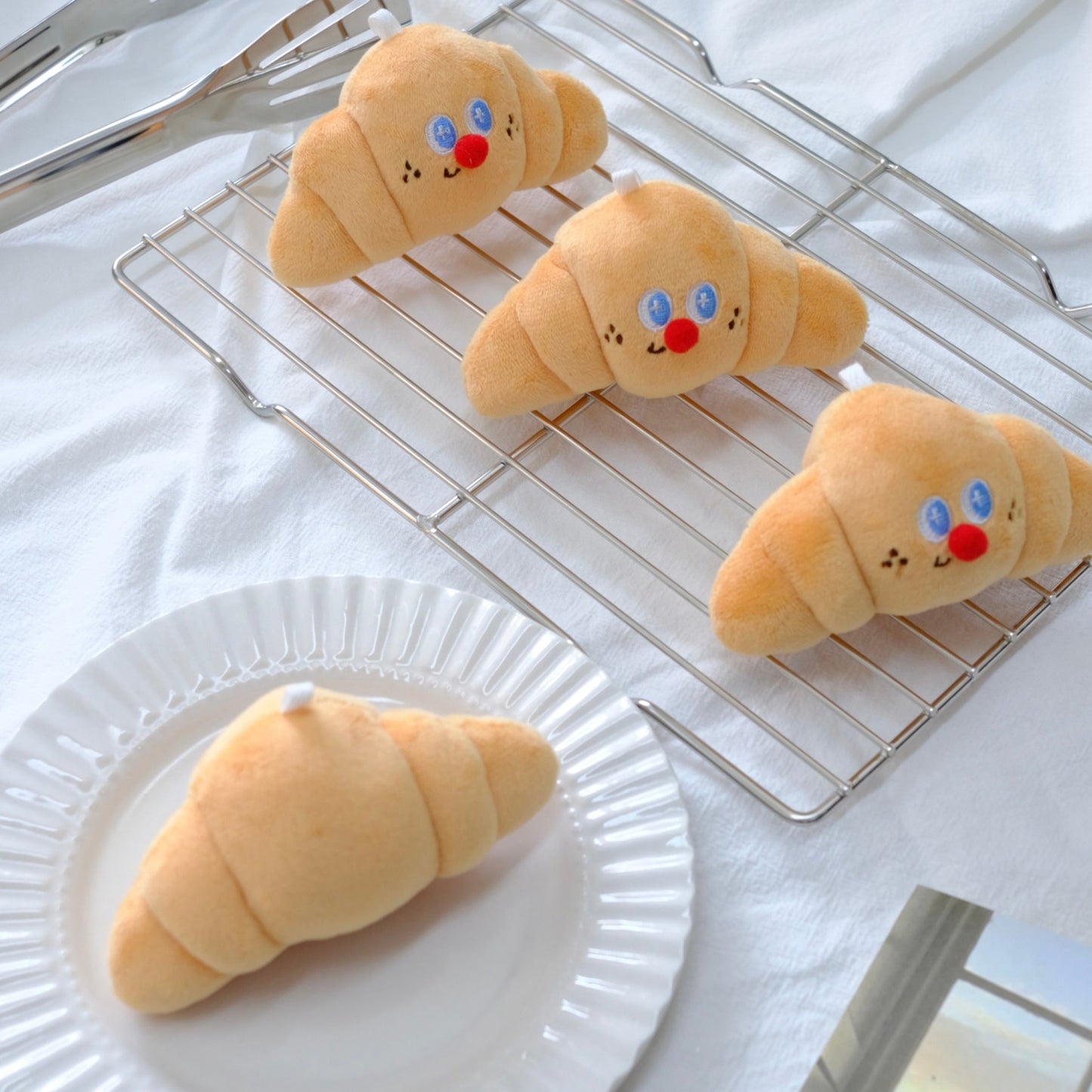 Plush croissants with face designs on a cooling rack and plate.