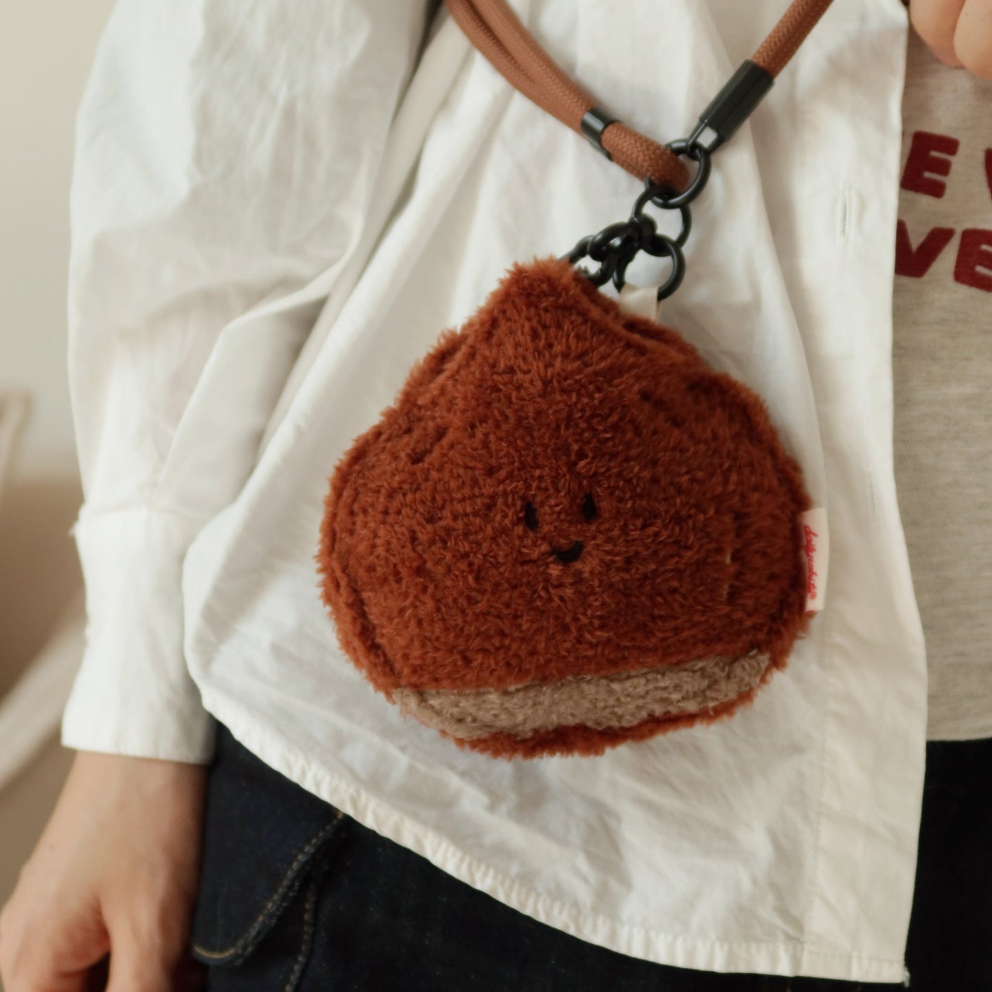 Person wearing a white shirt with a brown textured pouch on a strap over their shoulder.