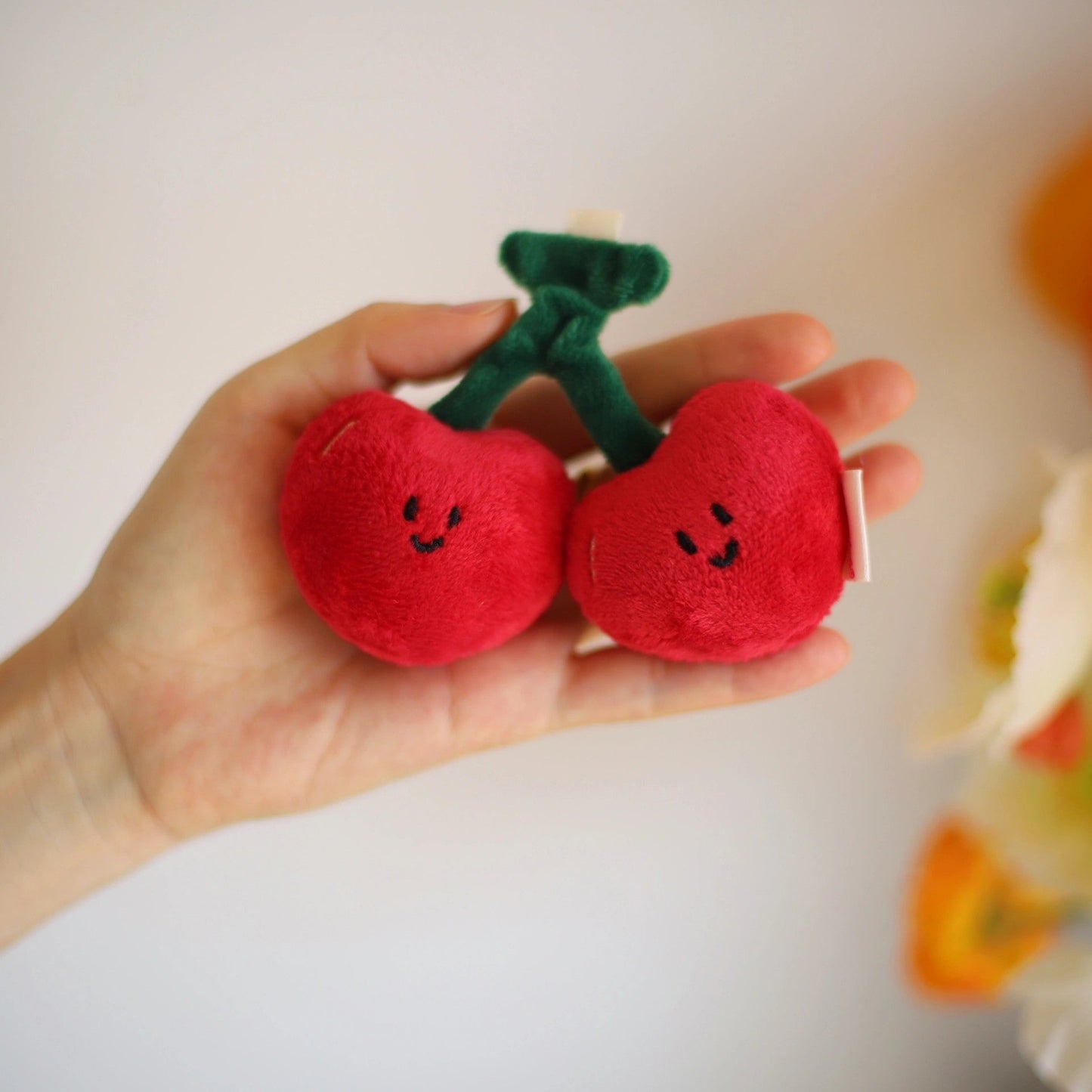 Hand holding two red plush cherries against a light background