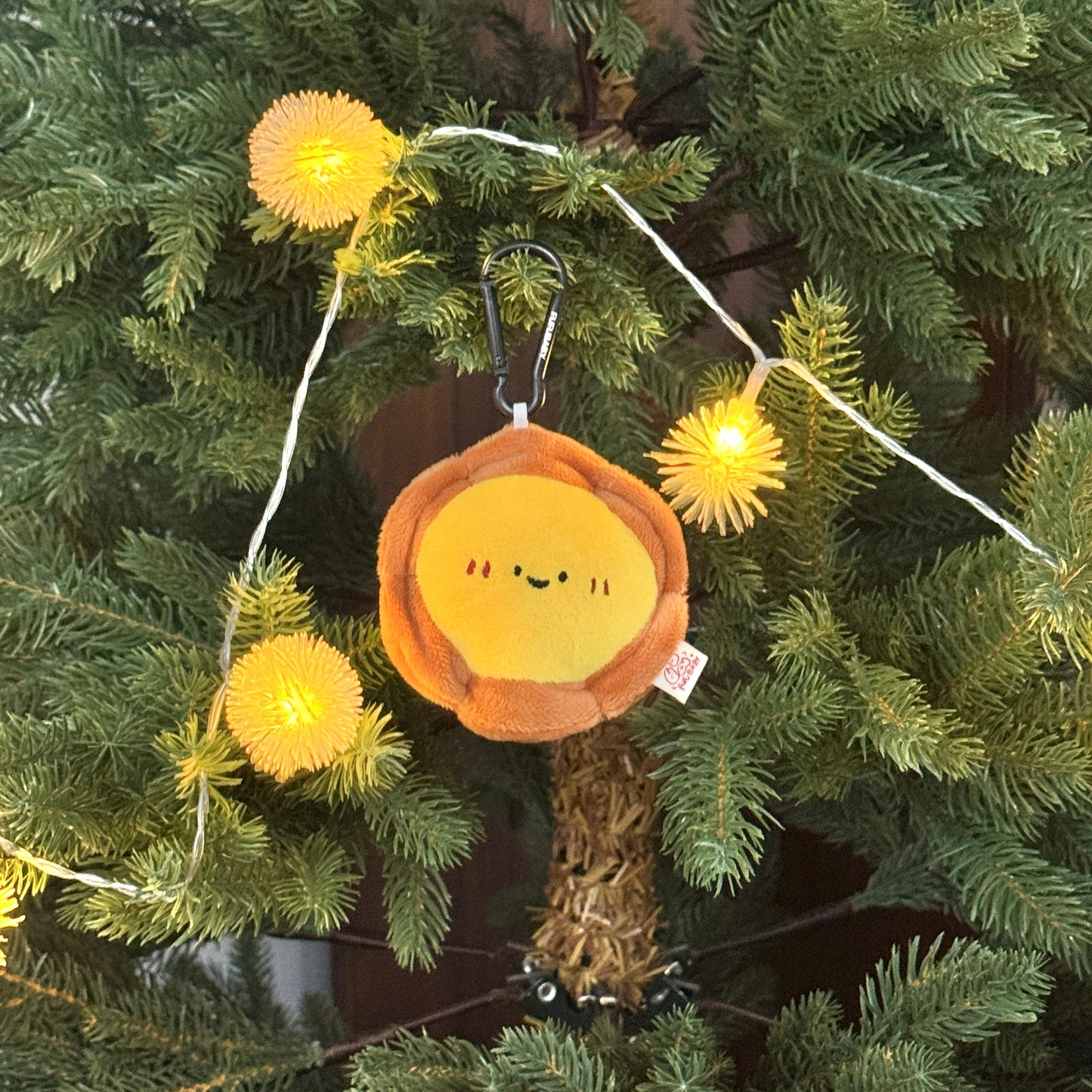 Decorative ornament with a smiling face on a string of lights hanging on a Christmas tree.