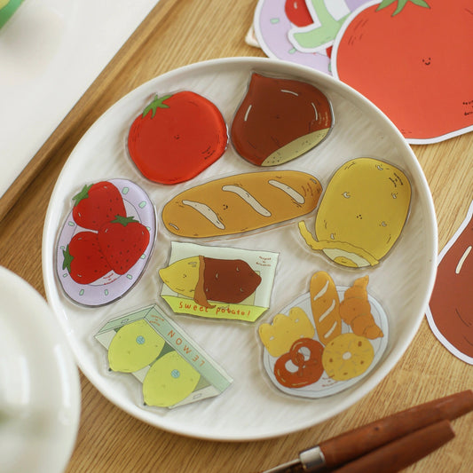 Colorful food-themed fridge magnets on a white plate with stickers in the background.