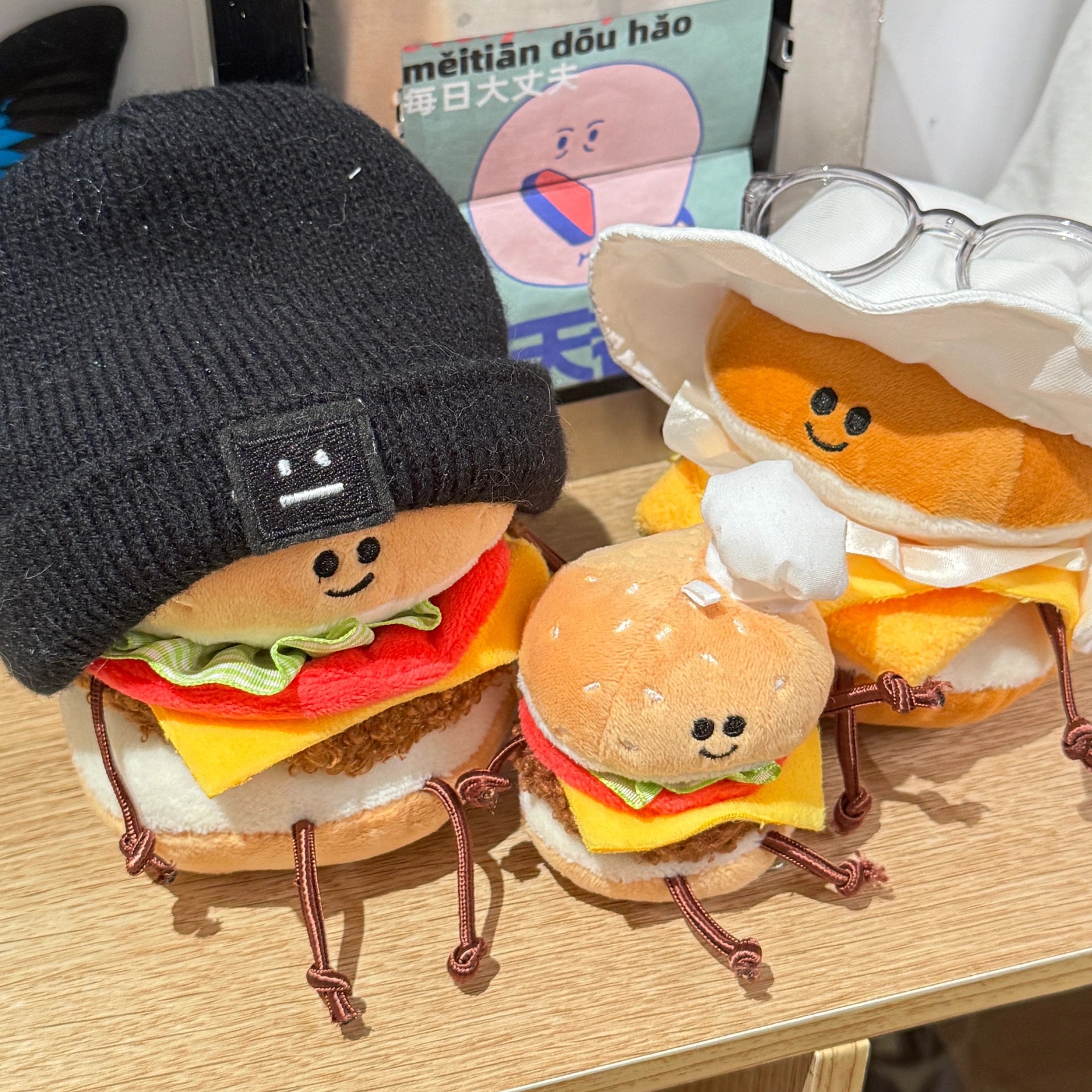 Plush toys shaped like hamburgers and buns on a wooden surface with a small box in the background.